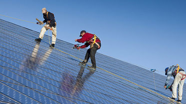 Monteure arbeiten mit Sicherungsgurten auf einer Solardachanlage unter blauem Himmel